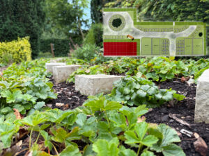 Grabstättenplan der Ruhegemeinschaft Kapellengarten mit eingezeichneten Grabstellen sowie ein Teil der Anlage mit Grabsteinen im Vordergrund auf dem Friedhof Garbsen-Horst.