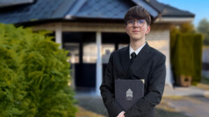Unser Auszubildender Nino Günsche steht vor der Kapelle in Osterwald. Das Bild ist teilweise KI-generiert. Nino stammt ursprünglich aus Chemnitz und ist für die Ausbildung nach Garbsen gezogen.