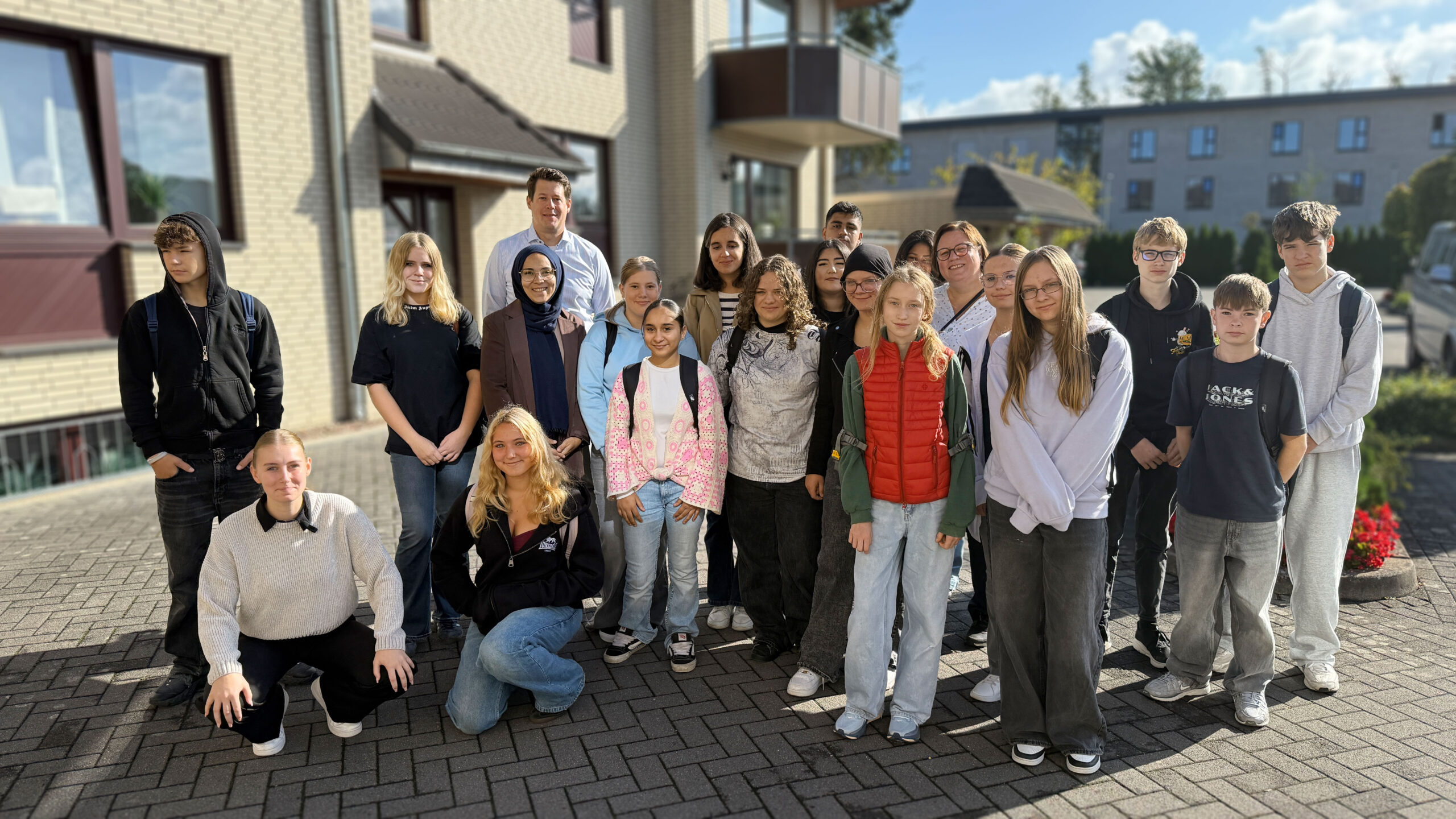 Schülerinnen und Schüler einer achten Klasse stehen gemeinsam mit Björn Henschel und Auszubildenden Pia Abraham vor dem Firmengebäude von Henschel Bestattungen in Garbsen-Berenbostel.